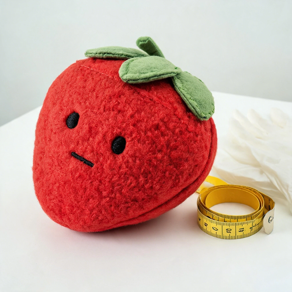Close-up inspection of embroidered eyes, reinforced seams, and securely sewn decorative leaves on a strawberry plush sample